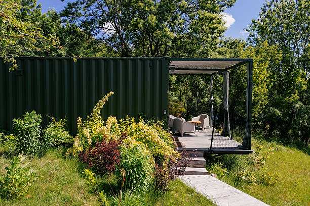 Modular house made from cargo shipping container features cozy outdoor seating area surrounded by vibrant plants. Architecture with serene atmosphere. Cozy home, landscape design, nature view concepts