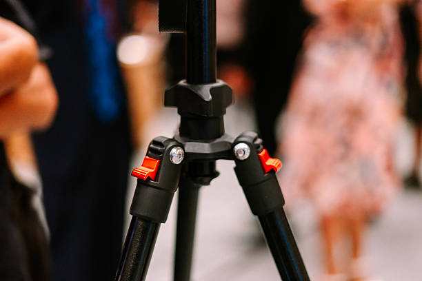 A close-up view of a sturdy black tripod with vibrant red locking mechanisms, perfect for stable photography or videography setups at events or studios. The blurred background emphasizes the