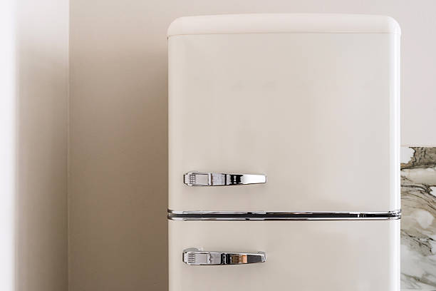 Close up shot of beige retro fridge stands against a neutral wall in a stylish and modern kitchen. Concepts of vintage household appliances and domestic equipment