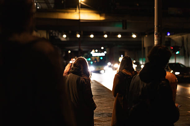 Berlin, Germany – November 11, 2025: People stand at a bus stop at night as headlights from approaching traffic illuminate the street under an elevated roadway. The scene shows passengers waiting for BVG line M43 in low light.