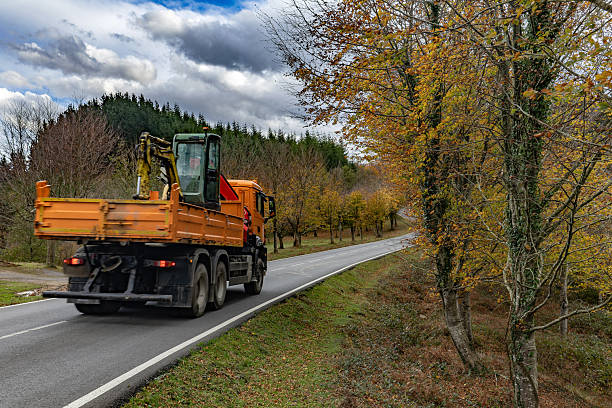 Spanish basque country. Orange dump truck hauling an excavator down a winding autumn country road through colorful forested countryside scenery