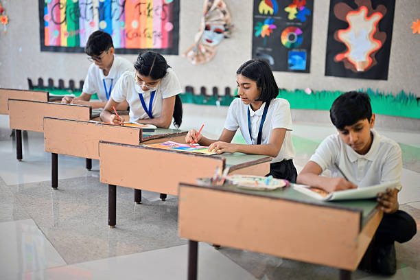 Students sit in a row sketching and coloring, each absorbed in their own drawing. Classroom walls display vibrant art and color wheels, adding a creative backdrop to the calm, concentrated scene.