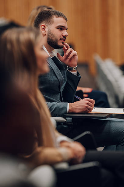 Audience member with beard attentively listening and taking notes on a notepad during a corporate seminar or lecture