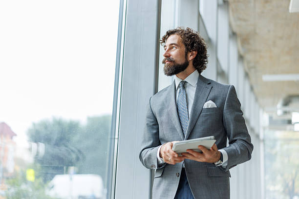 istock Businessman holding digital tablet looking at window thinking 2247004852