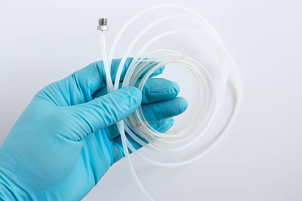 A scientist's hand in a blue glove holds flexible PEEK tubing with a stainless steel fitting. This is a component for an HPLC liquid chromatography system in a medical or science lab.