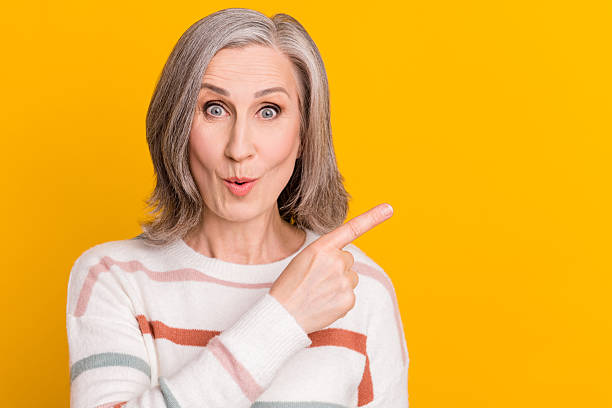 istock Photo of cute impressed lady pensioner wear striped pullover pointing finger empty space isolated yellow color background 2247016077