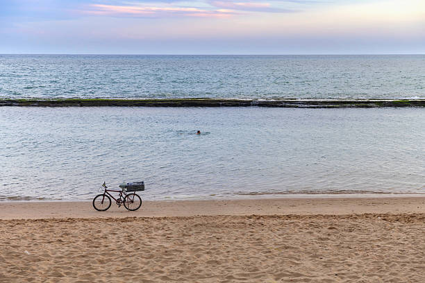 Recife, Brazil, November 25, 2024: A man swimms along the coast while his bicycle stands on the beach in this Brazil town on the late afternoon.