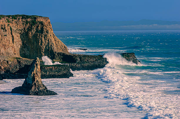 Ocean waves crashing on rocky cliffs and sandy beach, off California coast.Taken on Davenport Beach, California, USA.