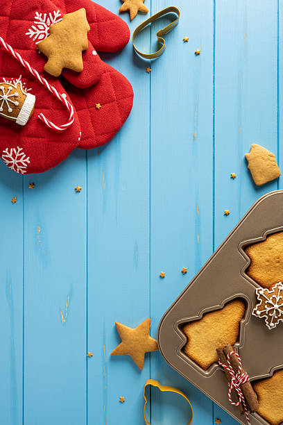Delightful top view vertical holiday scene featuring a red mitten, candy cane, cookie cutters, and baked treats on a cool blue wooden surface