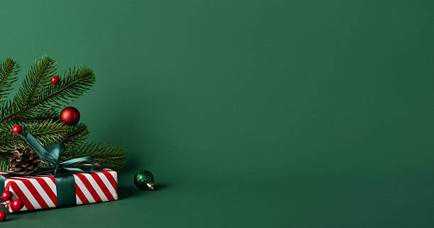 istock A green backdrop frames a festive Christmas gift with a pine sprig, red baubles, and a striped present, conveying holiday warmth, seasonal joy, and New Year celebration vibes 2247028480
