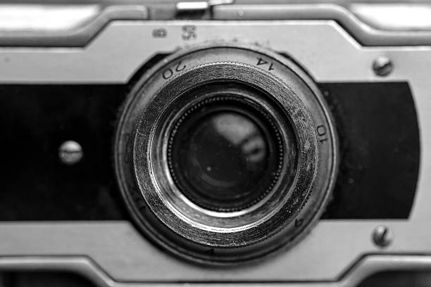 A detailed black and white macro photograph of a vintage camera lens, showcasing the worn metal textures, engraved numbers, and mechanical craftsmanship of classic analogue photography. The close-up perspective highlights the age, character, and engineering of old film cameras, making it perfect for themes of nostalgia, technology history, design, and mechanical detail.