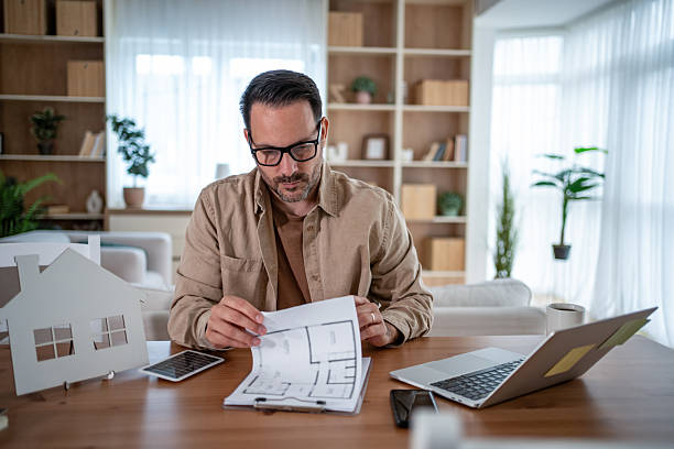 istock Man planning new home design with blueprints at desk 2247030821