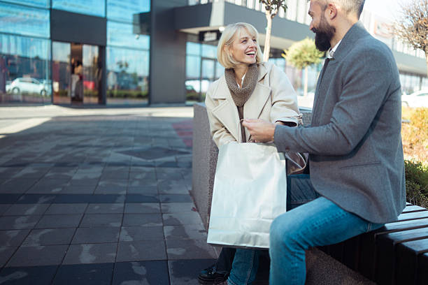 istock Couple resting after browsing stores, holding their shopping bags while chatting on a bench in an outdoor retail area 2247034758
