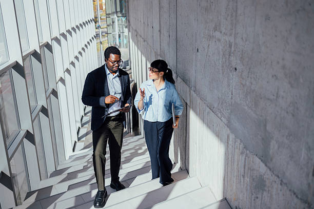 istock Business Professionals Walk and Talk on Modern Staircase Corridor in Corporate Office 2247035570