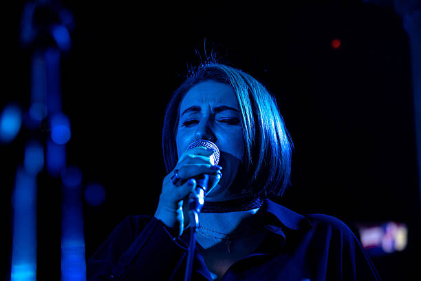Smiling young woman sitting and singing into a microphone, radiating positive energy as she performs with her acoustic band.