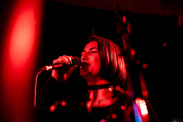 istock Young caucasian female singing with mic under red stage lights 2247039384