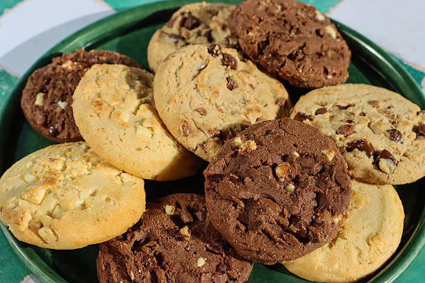 istock Full frame image of green plate with rounds of chocolate chip shortbread biscuits, festive holiday triple chocolate chip, milk chocolate chip and white chocolate chip cookies, white and green checked pattern background, elevated view, focus on foreground 2247039946
