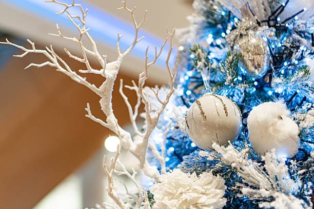Decorated Christmas tree with New Year elements, against an architectural backdrop Blue and silver ornaments on a tree illuminated by warm lights, creating a cozy ambiance No text present