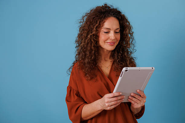 istock Smiling woman using tablet on blue background, connecting with digital technology for business or leisure 2247043696