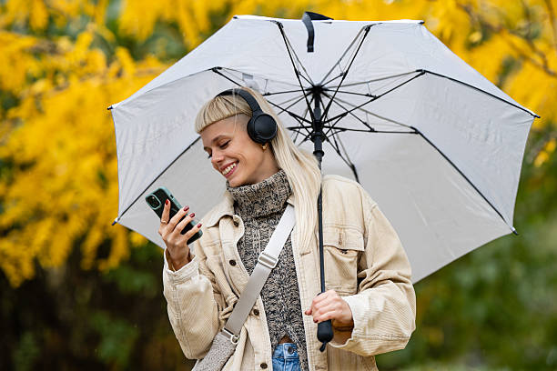 istock Smiling woman checking phone while walking in autumn rain 2247043735