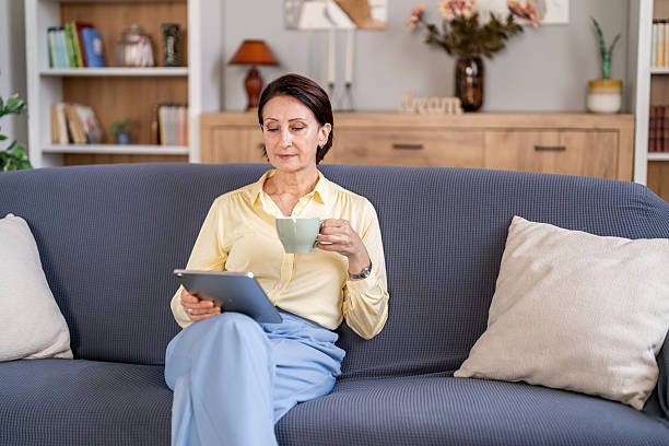 istock Senior woman relaxing at home reading digital tablet drinking coffee 2247045631