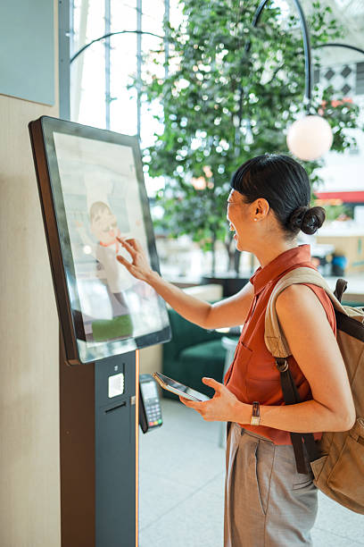 istock Young woman using self-ordering kiosk in restaurant: ordering food through touch screen technology 2247045716