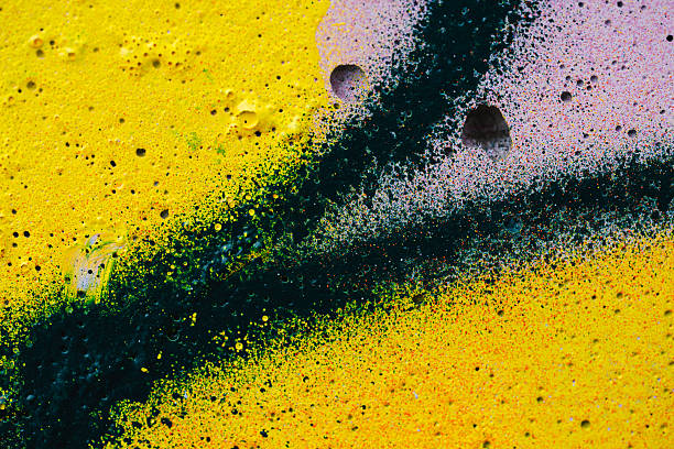 Close-up abstract view of a yellow painted wall featuring intersecting dark green spray-painted lines and scattered surface holes. The vivid colors, textured spray pattern, and natural imperfections create a dynamic, artistic background suited for creative design projects.
