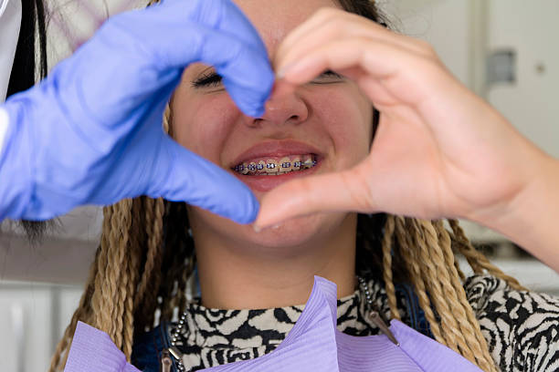 Young woman showing dental braces while patient and dentist hands form a heart shape, symbolizing caring orthodontic treatment, trust, successful dental care and happiness