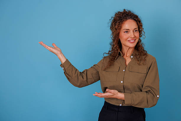 istock Smiling woman presenting new information with open hands, showing copy space against a blue background 2247050294