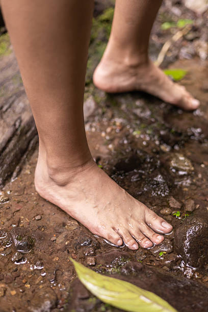 Close-up of a woman’s bare feet standing on wet river stones. The scene highlights the natural texture of the rocks and the refreshing feel of flowing water during an outdoor nature session.
