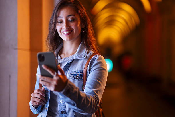 istock Smiling Woman in Denim Jacket Using Smartphone in Warmly Lit Tunnel Corridor 2247052145