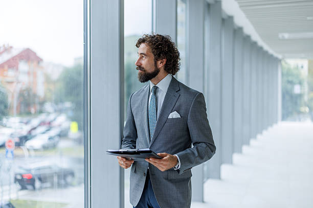 istock Businessman looking out window holding clipboard thinking 2247074098