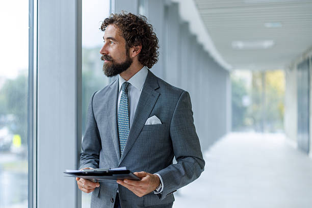 istock Professional businessman holding clipboard looking through office window 2247074112