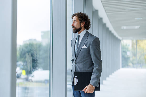 istock Thoughtful businessman holding clipboard standing by office window 2247074115