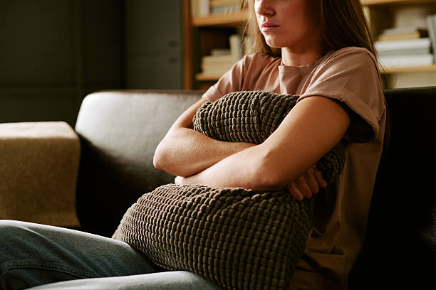 Young Caucasian Woman Sitting on Sofa Hugging Pillow Feeling Anxious Indoors