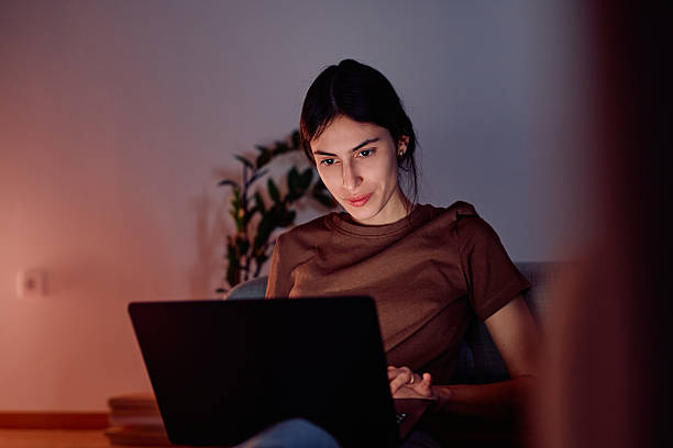 istock Young woman working remotely on laptop at night 2247081906