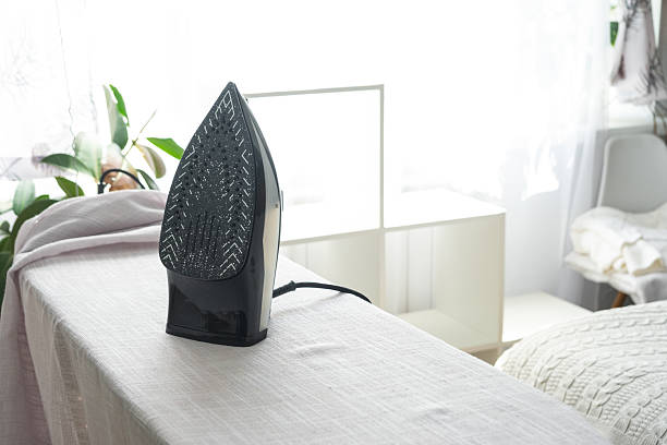 The iron is on the ironing board with a plain cloth in the room in close-up.