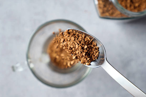 istock Freeze-dried instant coffee beans falling from a metal teaspoon into an empty cup on background of table with coffee glass jar. 2247082818