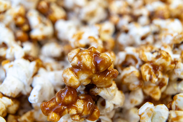 Macro view of freshly made caramel popcorn, highlighting the glossy caramel coating. Shot on a kitchen counter, this image captures the texture and warmth of a homemade treat.