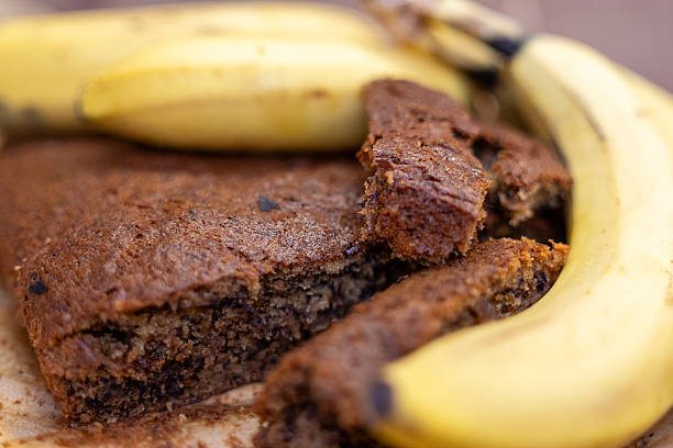 Close-up of a slice of homemade banana bread with fresh banana on the side. The moist texture and banana pieces are visible, captured on a wooden cutting board in a home kitchen.