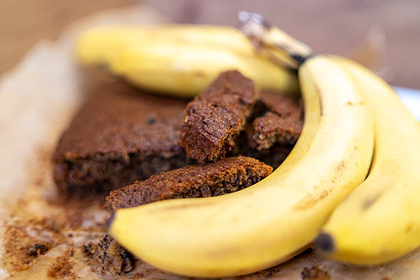 Close-up of a loaf of homemade banana bread next to ripe bananas. Macro photography captures the texture, color, and warmth of a freshly baked treat in a cozy home environment.