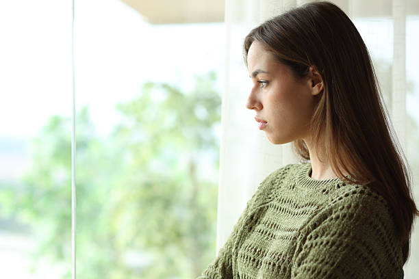 istock Sad woman in green looking through a window at home 2247087132