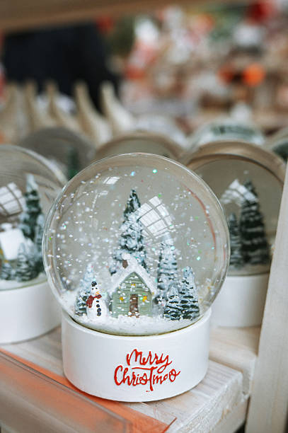 Festive holiday snow globe with cottage and snowman scene.
