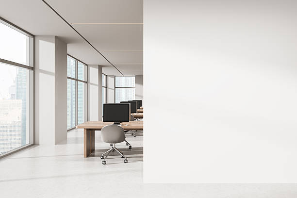 istock Open space office with row of workstations and large blank wall for advertising or poster mockup concept in modern high-rise interior setting. 3D Rendering 2247087910