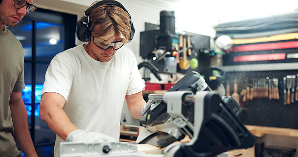 istock Creative, artisan and men with machine, workshop or cutting plank with gloves, woodwork and process. Carpentry, manufacturing and person with equipment for furniture production, tools and warehouse 2247097186