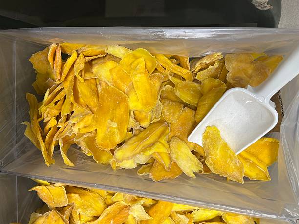 Dried mango slices in a clear container, showcasing vibrant yellow hues and natural textures, with a scoop resting on top, representing healthy snacking options