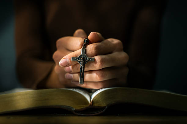A woman holding rosary beads in prayer over an open Bible, seated in a dimly lit church, symbolizing deep Christian faith.
