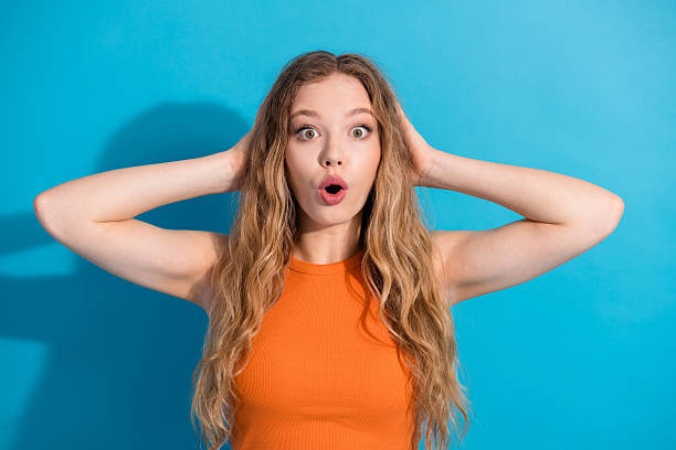 istock Glamorous young woman in orange top with surprised expression against blue background showcasing fashion lifestyle beauty and shopping appeal 2247100481
