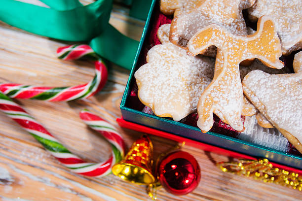 Assorted Christmas cookies shaped like angels, stars, and trees, candy canes, ornaments, and ribbon on rustic wooden surface, festive holiday food and decoration concept.
