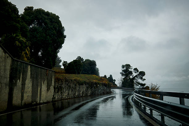 A moody and atmospheric view of narrow mountain roads on a rainy, fog-covered day. Wet asphalt, low visibility, and dense greenery create a sense of isolation and quietness, typical of high-altitude rural routes. Ideal for themes related to travel, weather conditions, remote landscapes, transportation challenges, and scenic mountain environments.